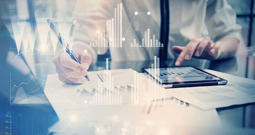 Hands working with a pen and tablet over financial charts in a bright office.