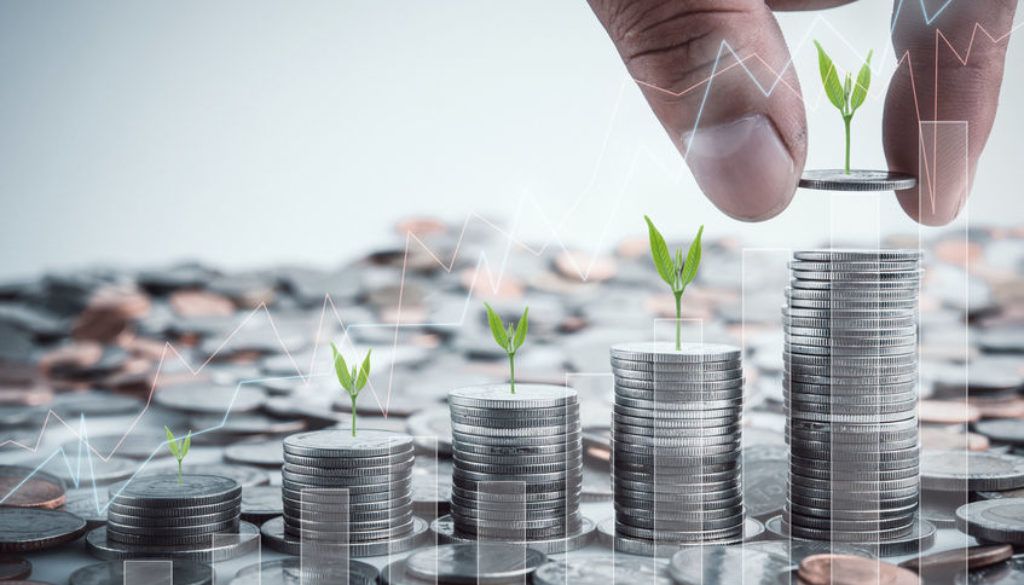 Hands stacking coins into growing columns with green sprouts, symbolizing financial growth and investment
