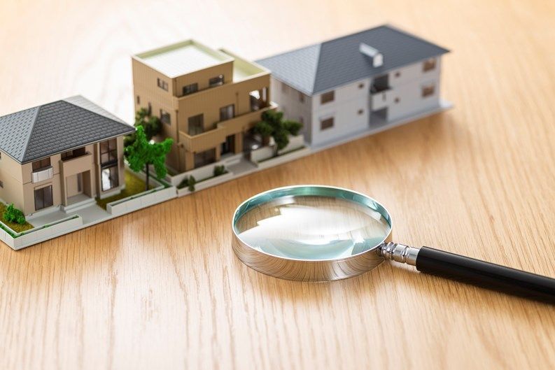 Magnifying glass over miniature houses on a wooden table, suggesting home inspection or real estate search