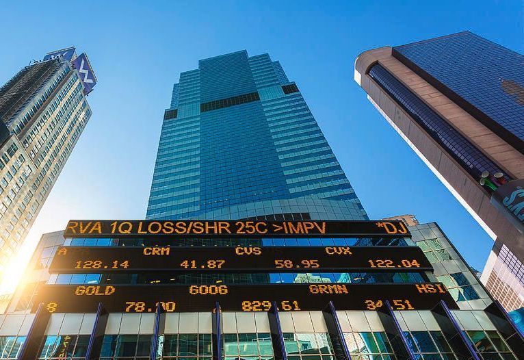 Downtown skyscrapers with a digital stock ticker board in front, seen from a low angle under blue sky