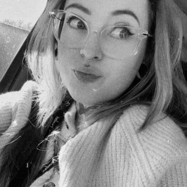 Woman wearing glasses, lip piercing, looking askance, making a face, sitting in car.