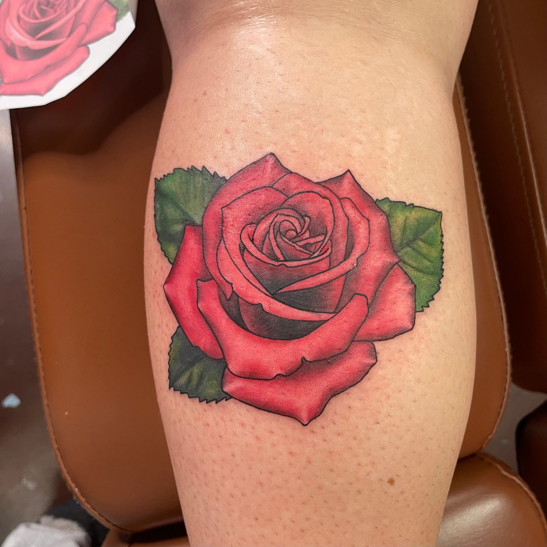 Red rose tattoo on a leg, with green leaves and a tattoo stencil visible.