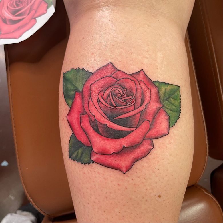 A red rose tattoo on a leg, with green leaves and a black outline.