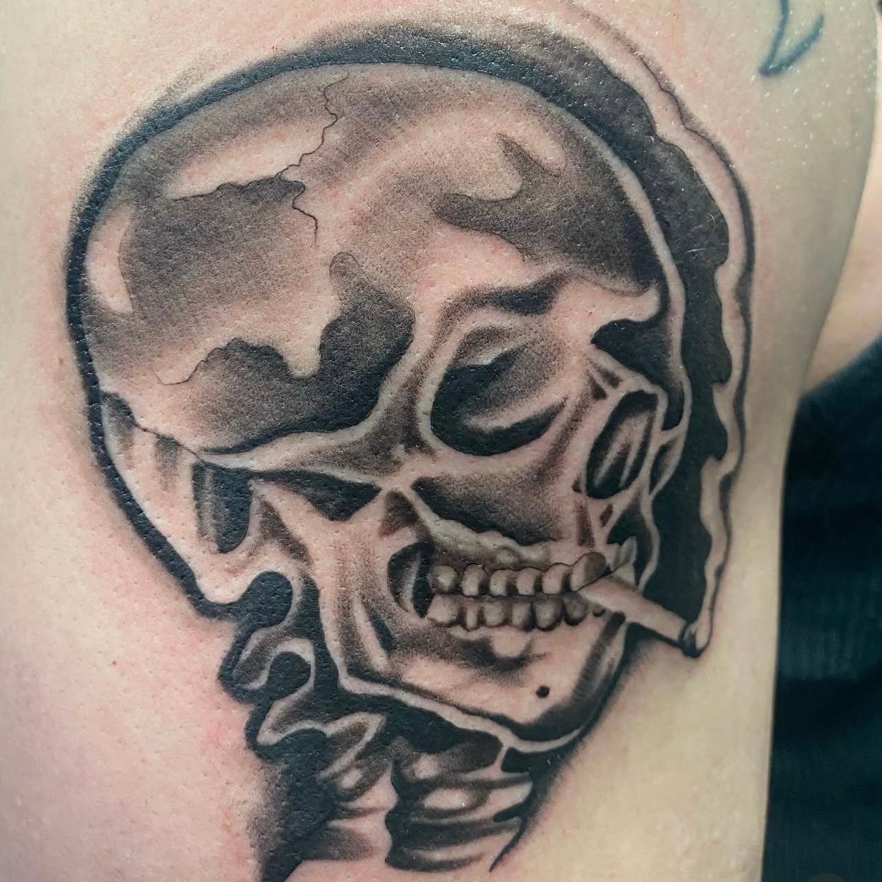 Skull tattoo with a cigarette, shaded in black and gray.