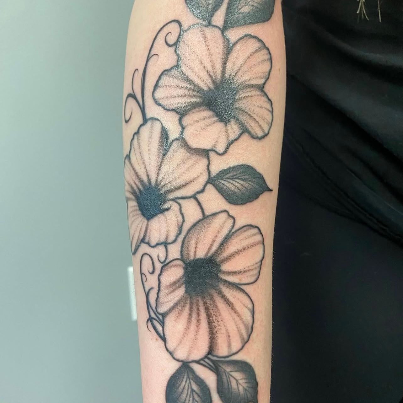Tattoo of three stylized flowers with dark centers and leaves on a forearm.