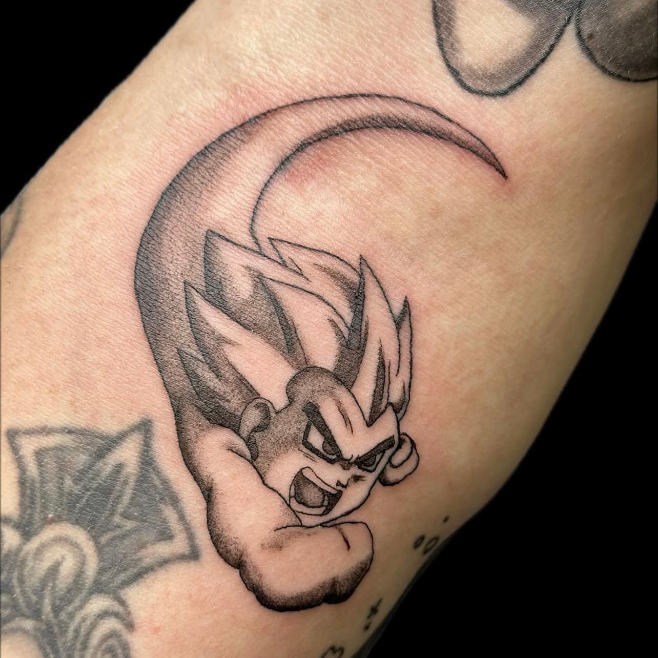 Black tattoo of a Dragon Ball character in a power-up pose, on a person's arm.