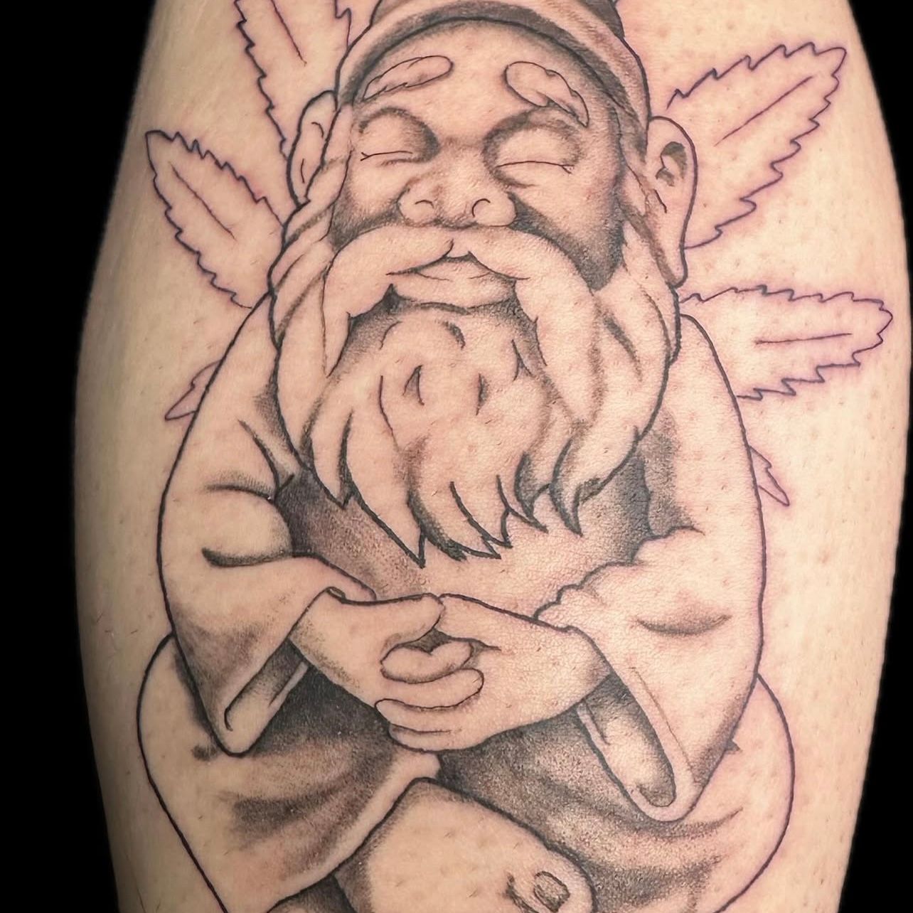 Tattoo of a meditating gnome with a long beard, hands clasped, and cannabis leaf outline.