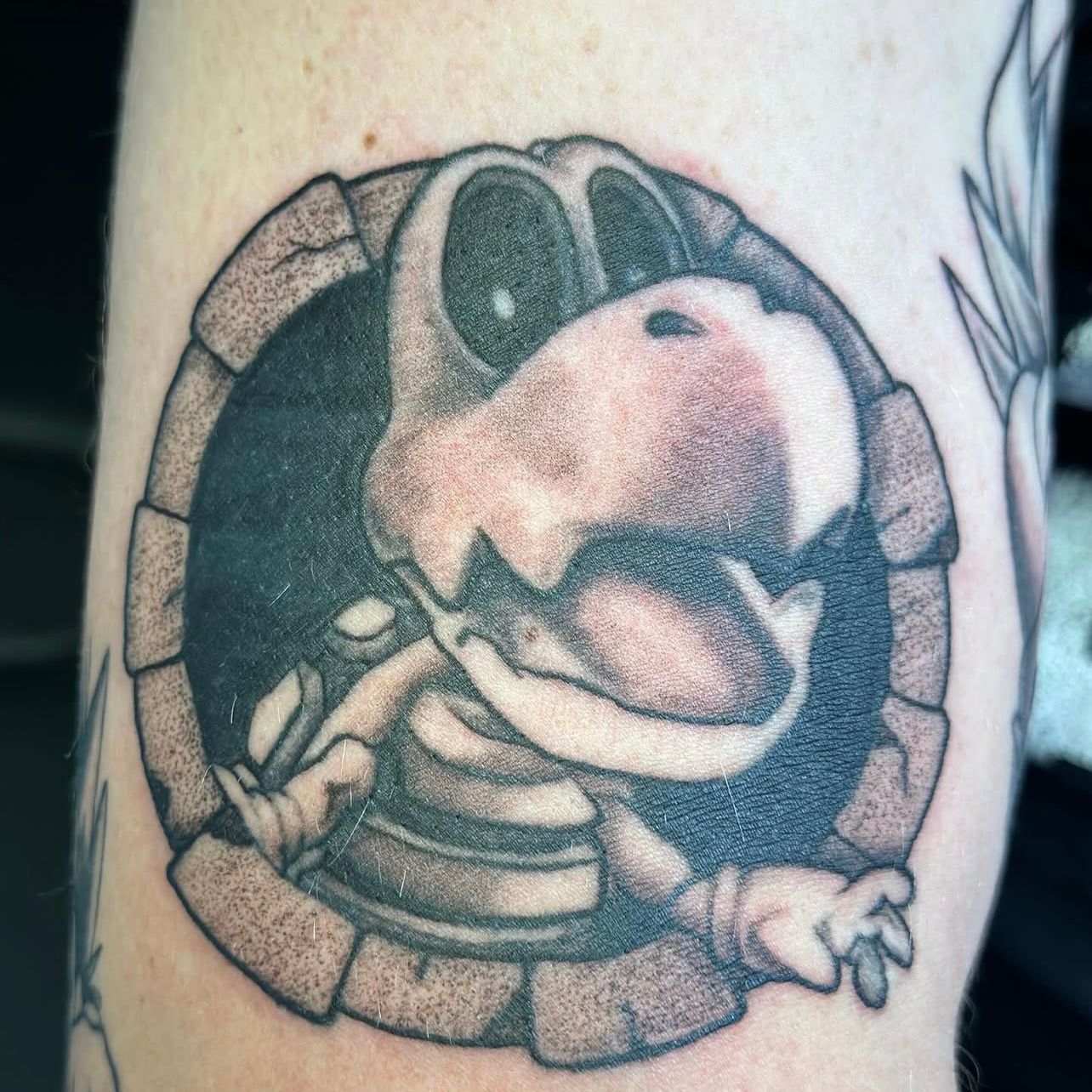 Black and gray tattoo of a Dry Bones from Super Mario peeking out of a stone circle.
