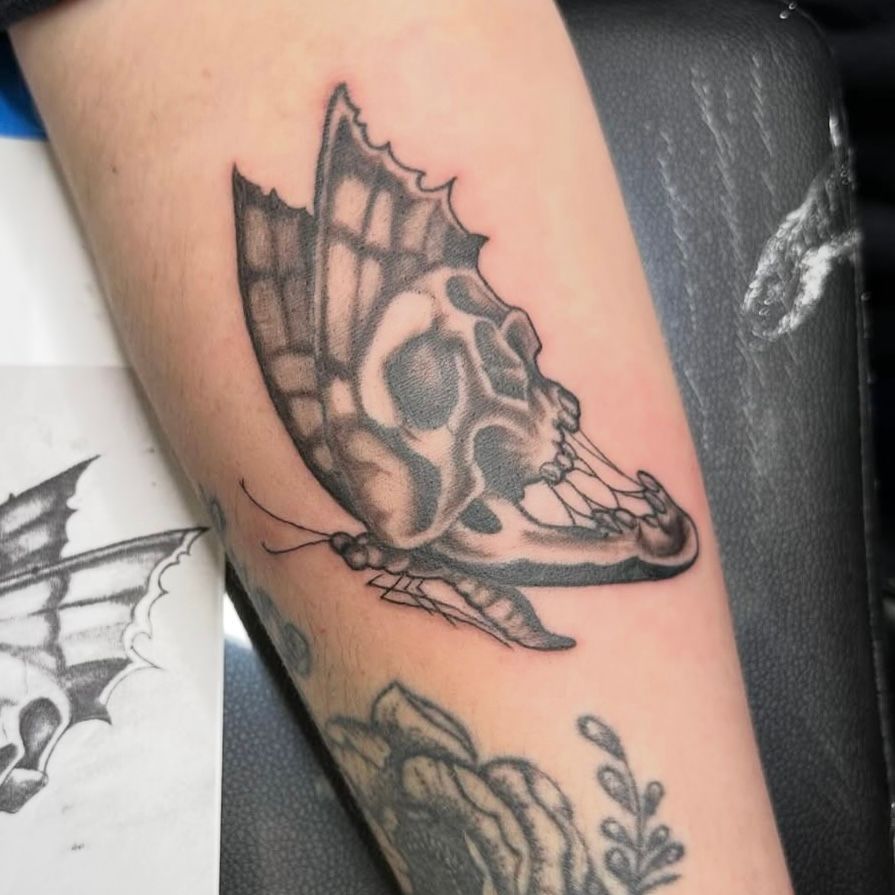Tattoo of a skull-shaped butterfly on an arm, black and gray ink, with detail.