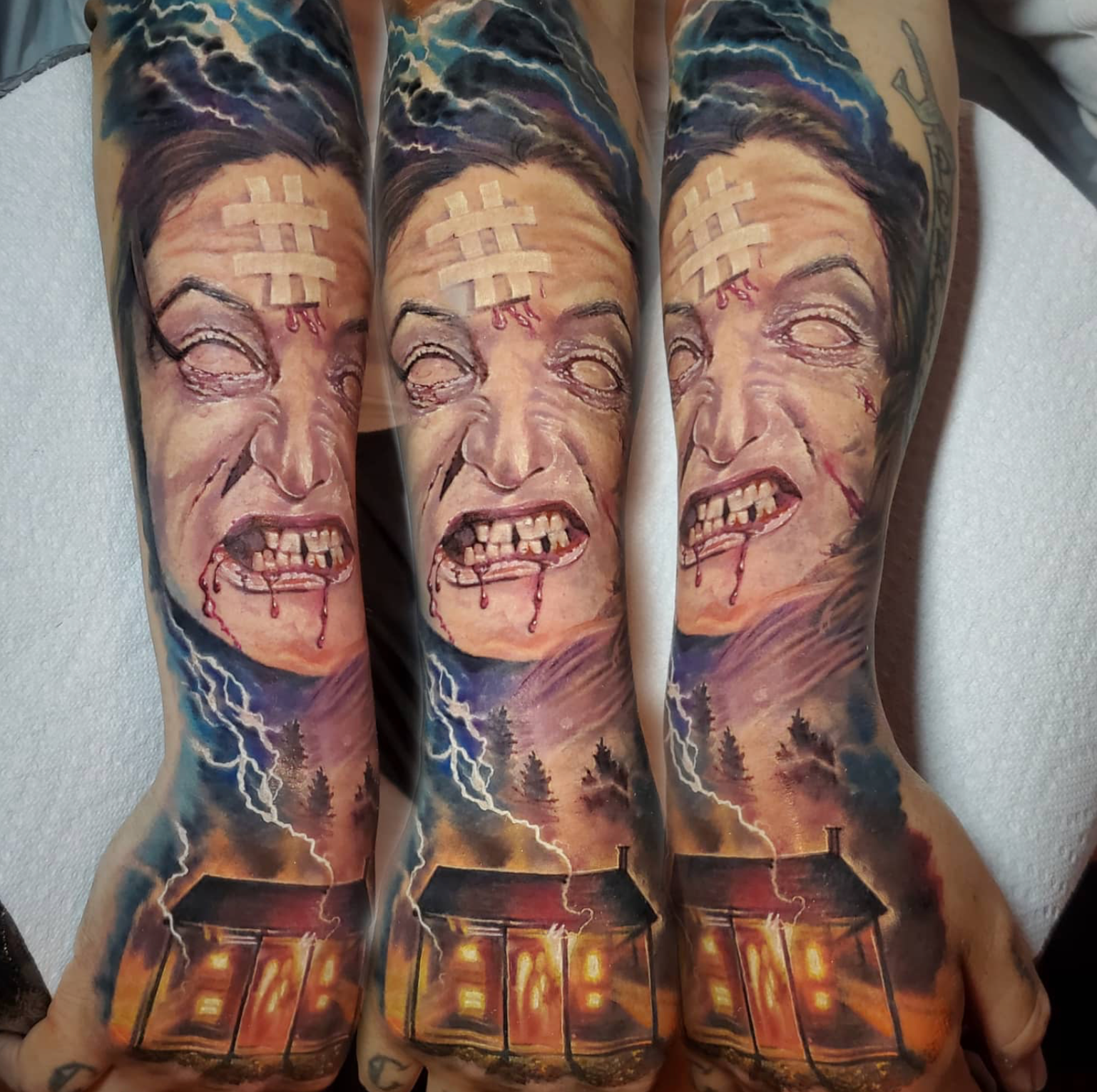 Zombie arm tattoo: woman with bloody mouth, lightning, house, and trees in a stormy sky.