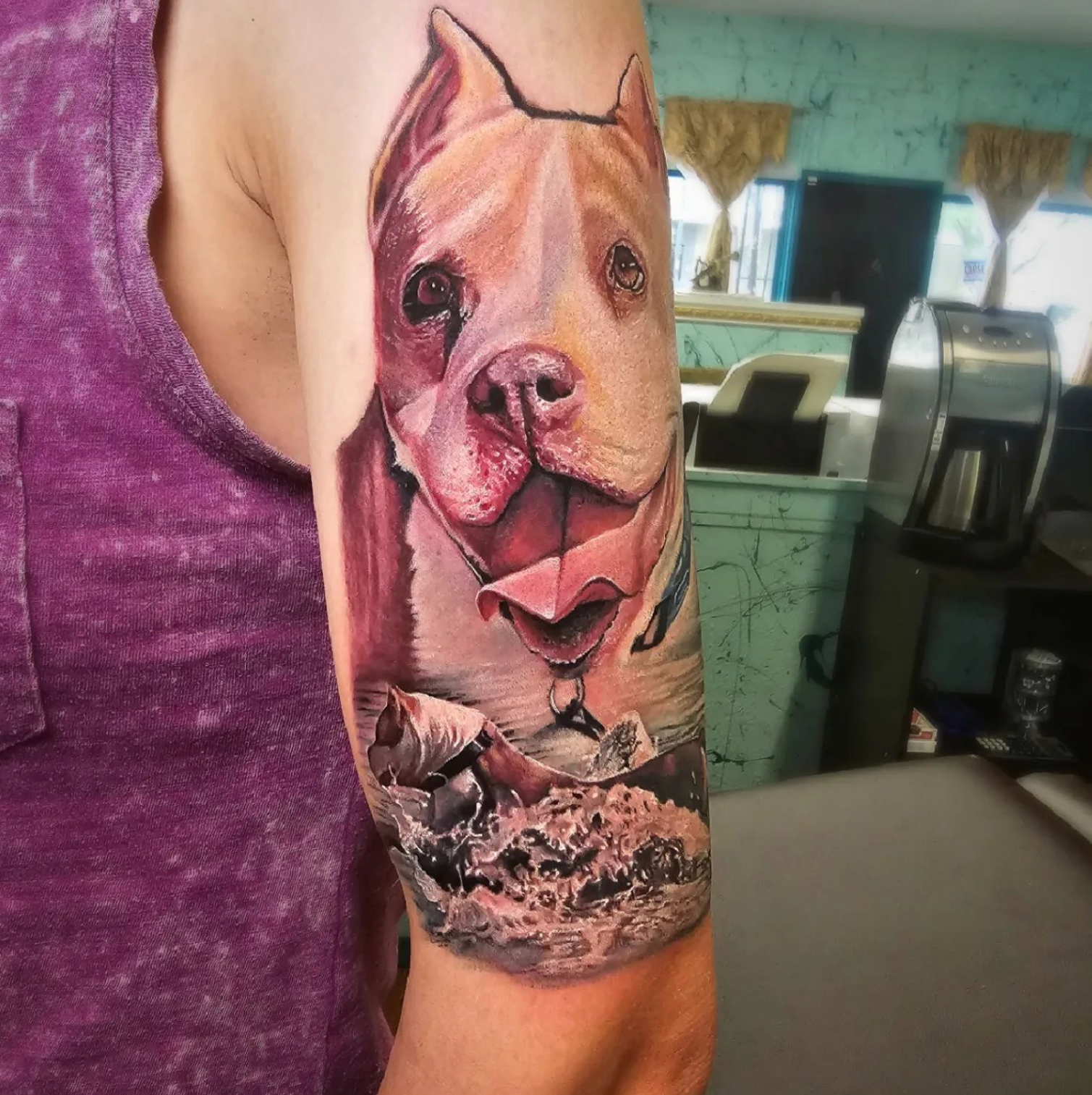 Tattoo of a pit bull dog with open mouth on forearm, mostly tan and white with rocks at bottom.