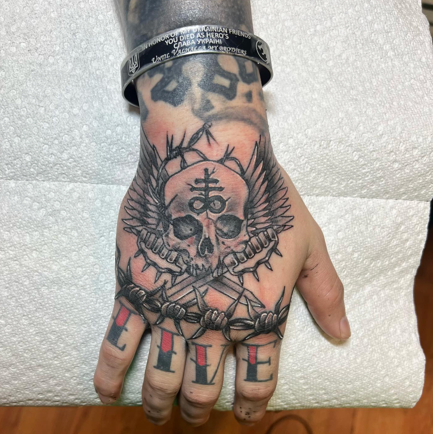 Hand tattoo: Skull with wings, barbed wire, 
