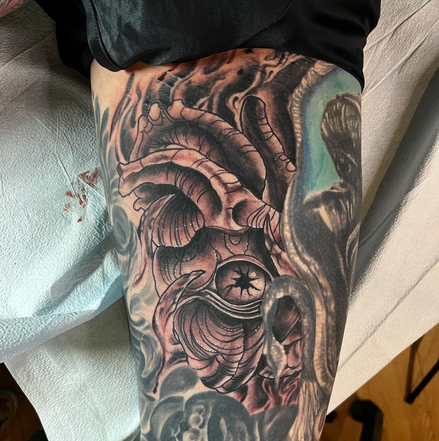 Tattoo of a detailed, gray, stylized heart with a central eye on a forearm, surrounded by smoky elements.