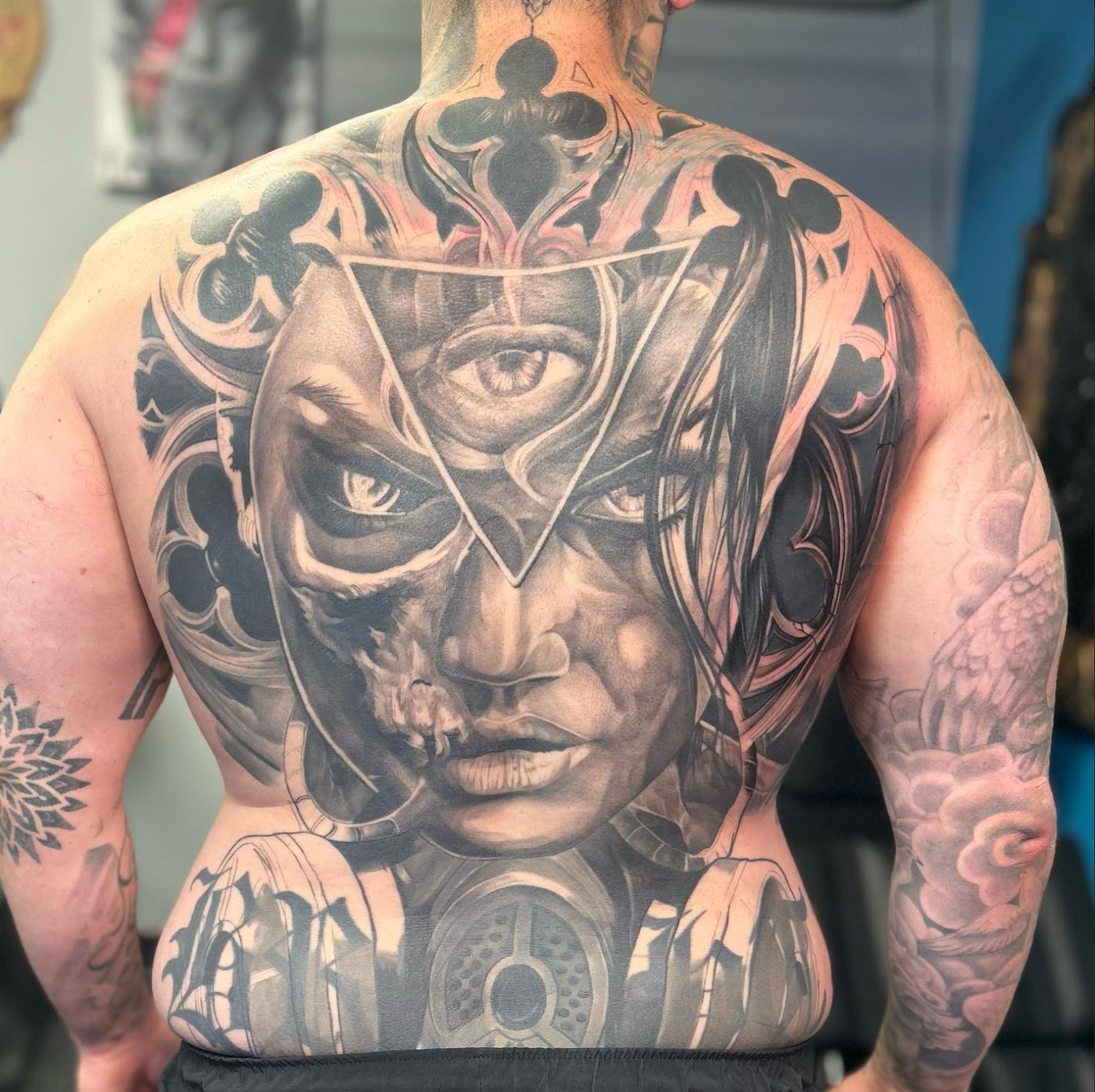 Tattoo on a person's back, a gothic-style face with an eye within a triangle. Detailed and grayscale.