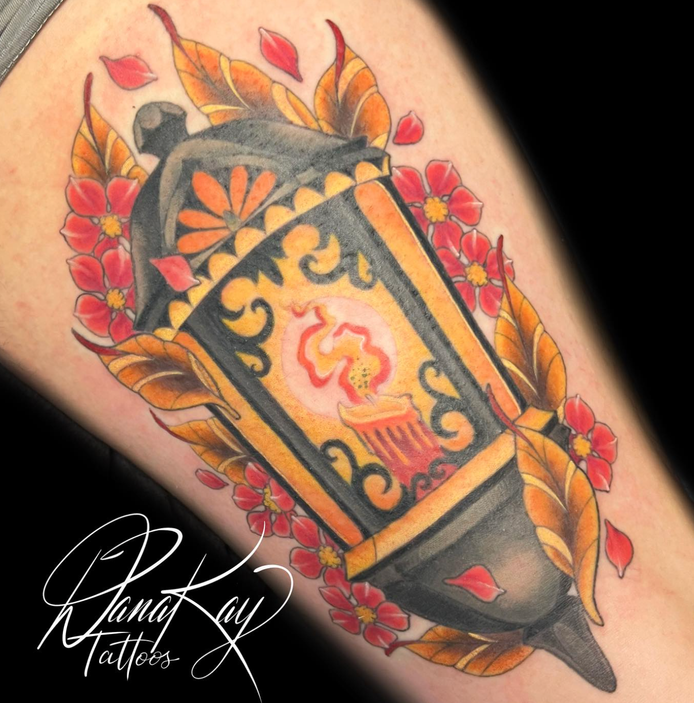 Tattoo of an ornate lantern with a lit candle, surrounded by red flowers and orange leaves.