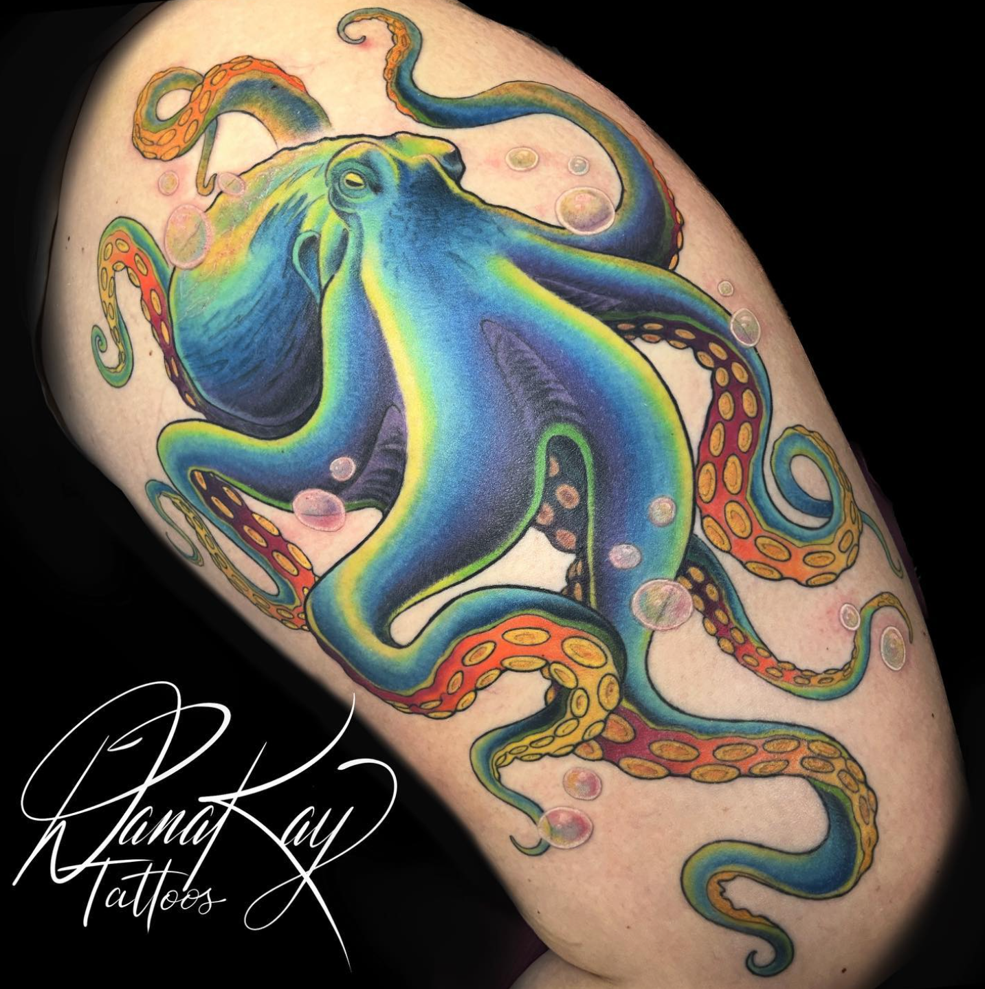 Colorful octopus tattoo on skin, with blue, orange, and yellow hues. Bubbles surround it.