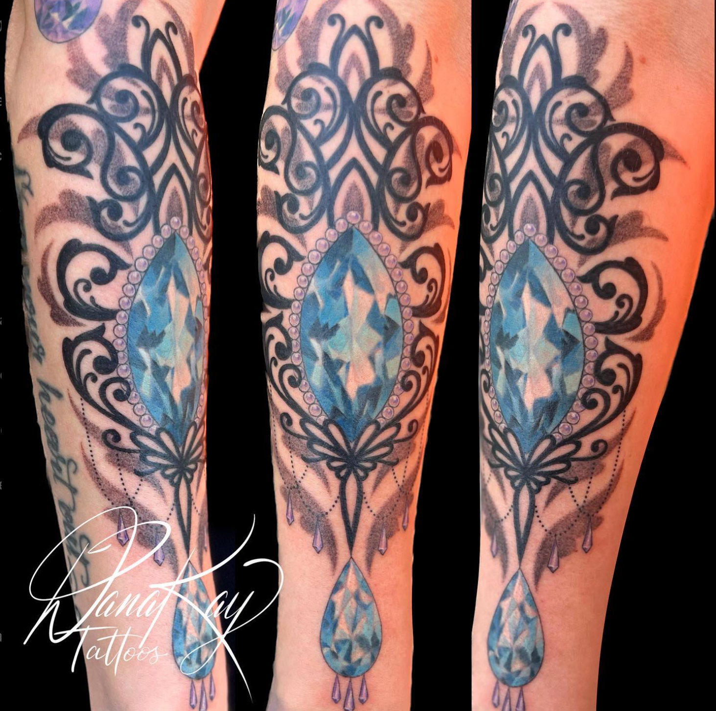 Tattoo of a blue gem design on an arm with ornate black filigree and teardrop accents.