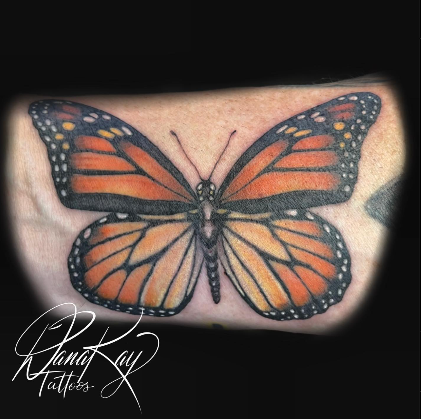 Monarch butterfly tattoo in orange, black, and white on skin.