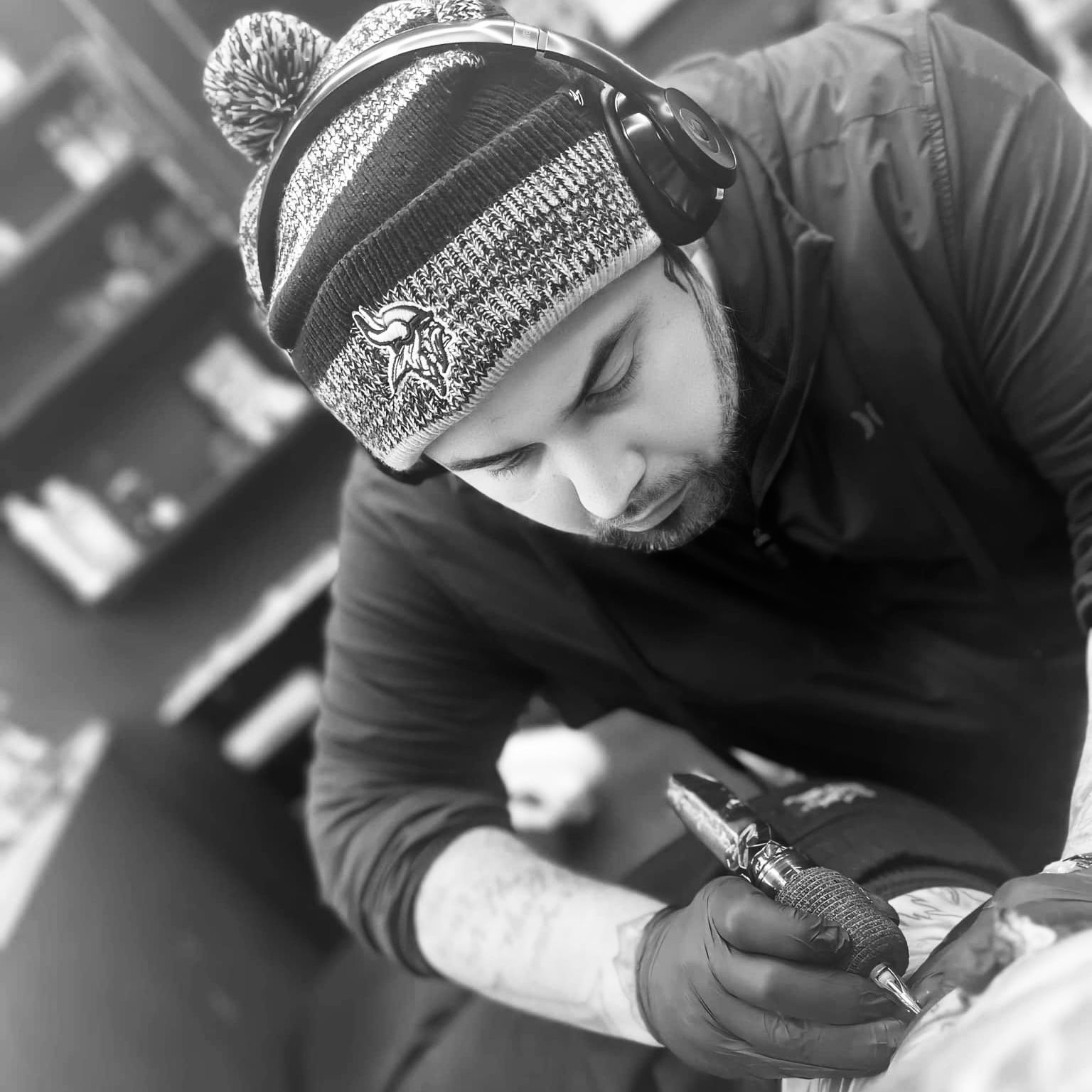 A person in a knit hat tattooing someone's arm, indoors.