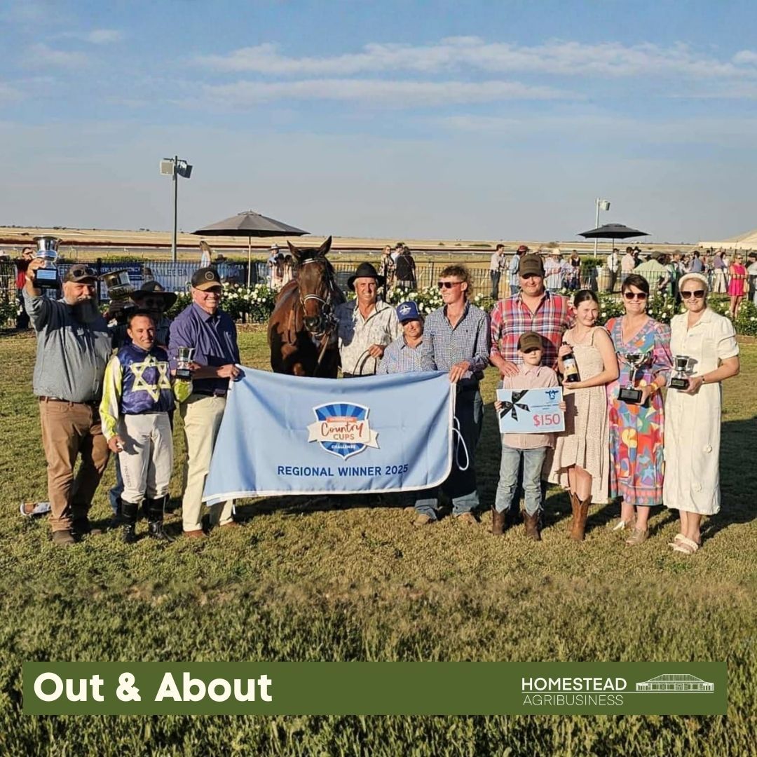 Group holding a banner in a grassy field at an outdoor event under a clear sky.