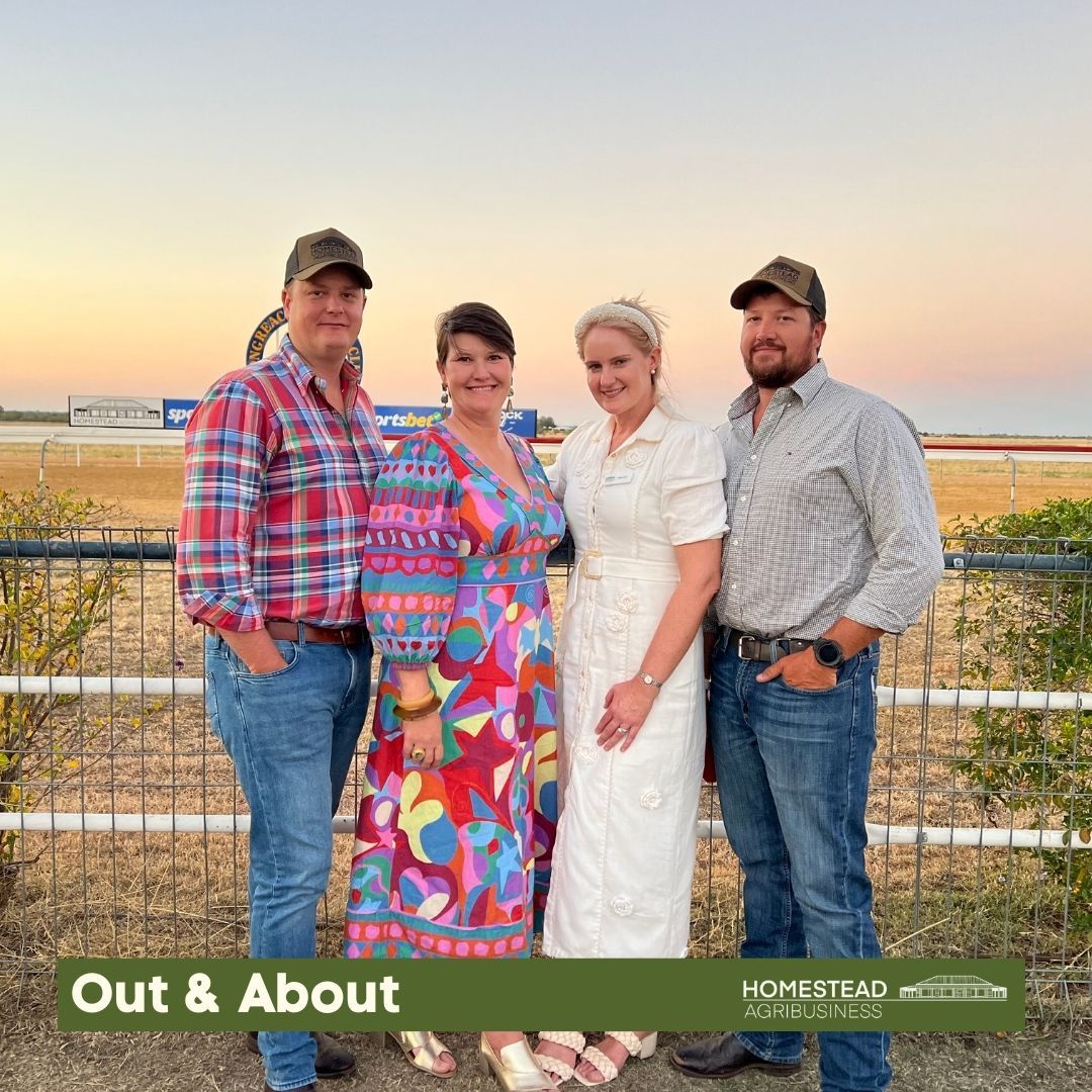 Four people stand together outdoors at sunset, with a field and fence behind them.