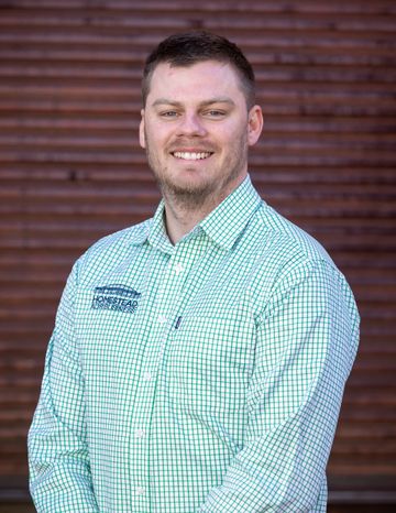 Hugh from Homestead Agribusiness in a green checkered shirt standing in front of a brown shuttered wall