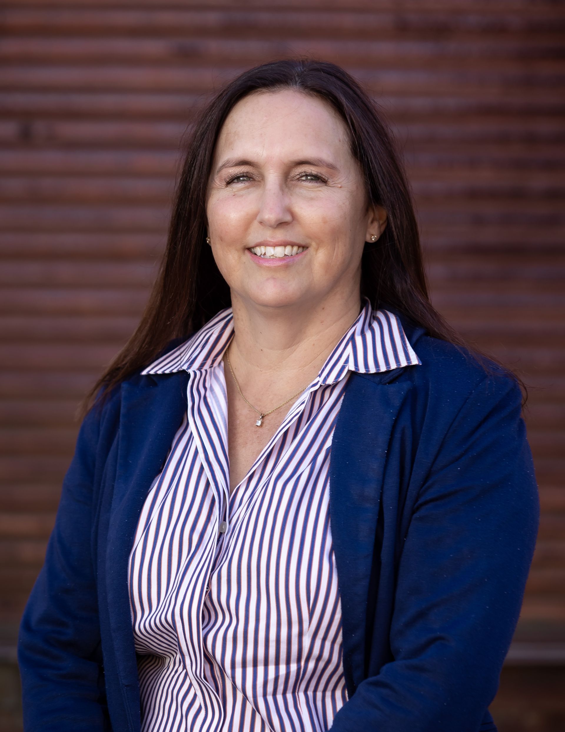 Marsha from Homestead Agribusiness in a navy blazer and striped shirt against a blurred brown background.
