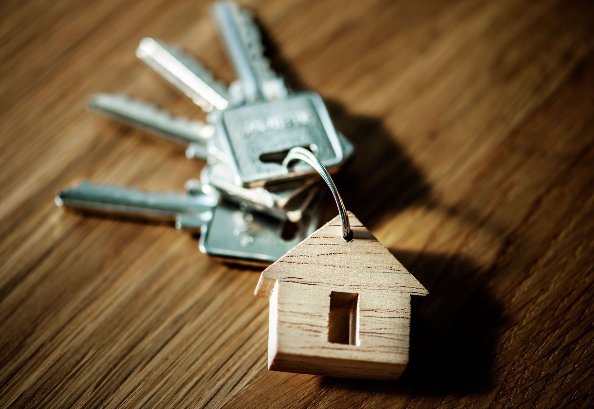 Small wooden house keychain beside a set of metal keys on a wooden surface