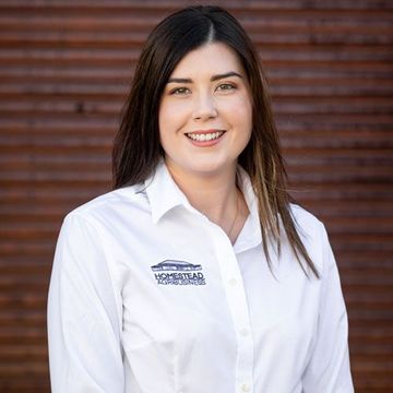 Brianna from Homestead Agribusiness  in a white shirt against a wooden wall background