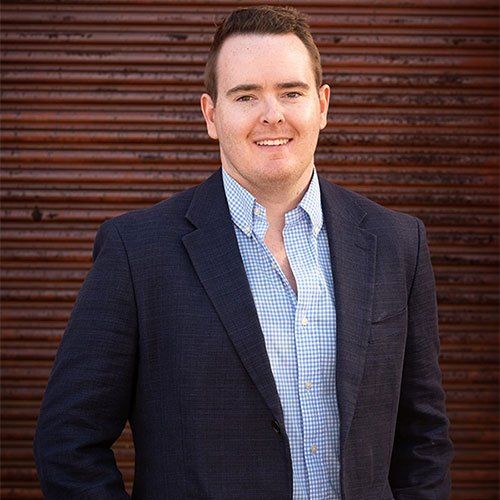 Luke Radford from Homestead Agribusiness in a dark blazer and blue checkered shirt standing before a corrugated metal wall