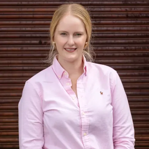 Portrait of  Stephanie from Homestead Agribusiness in a light pink shirt standing before a brown slatted wall