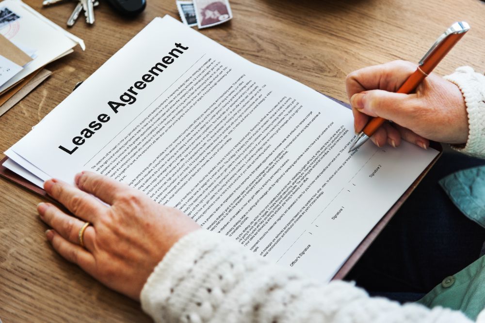 A person is signing a lease agreement on a wooden table.