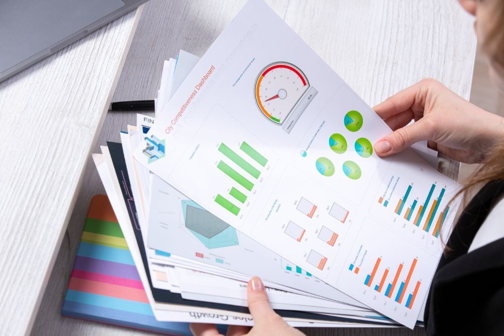 A woman is holding a stack of papers with graphs on them.