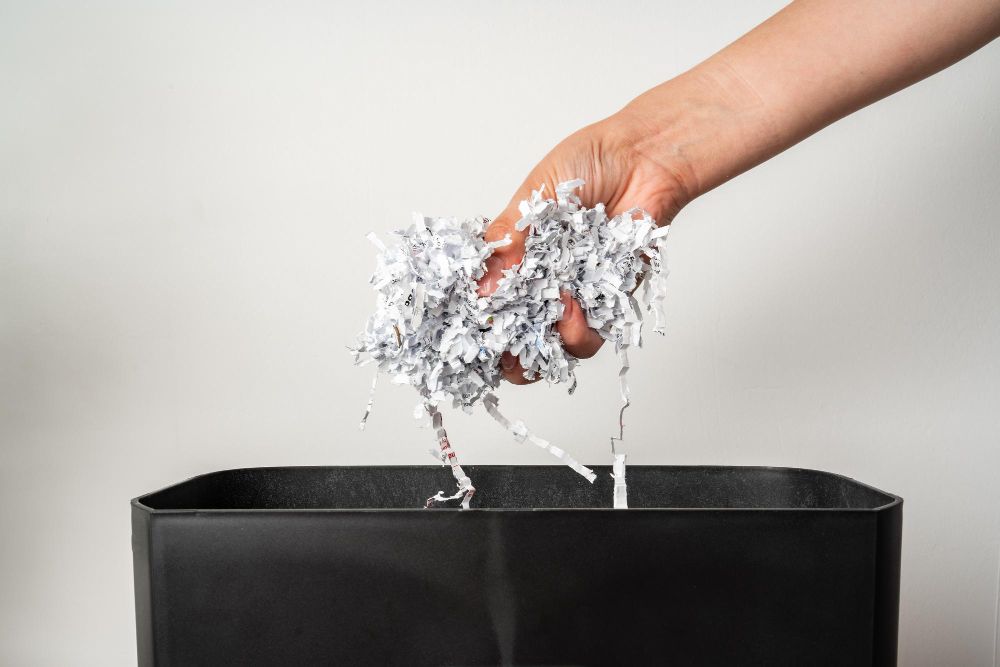 A person is throwing shredded paper into a trash can.