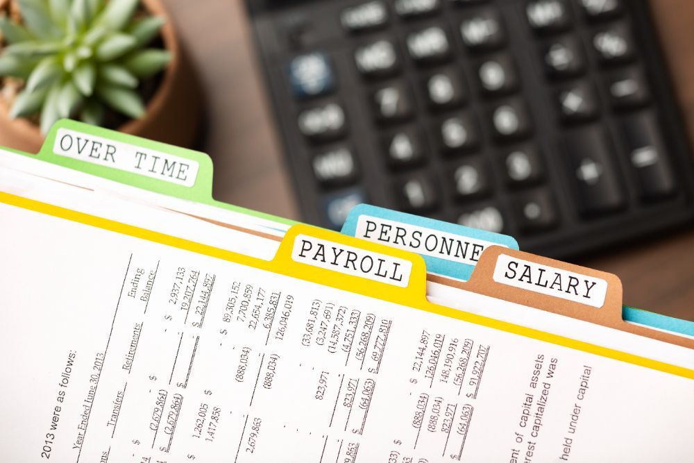 A calculator is sitting on a table next to a folder with tabs for payroll and salary.