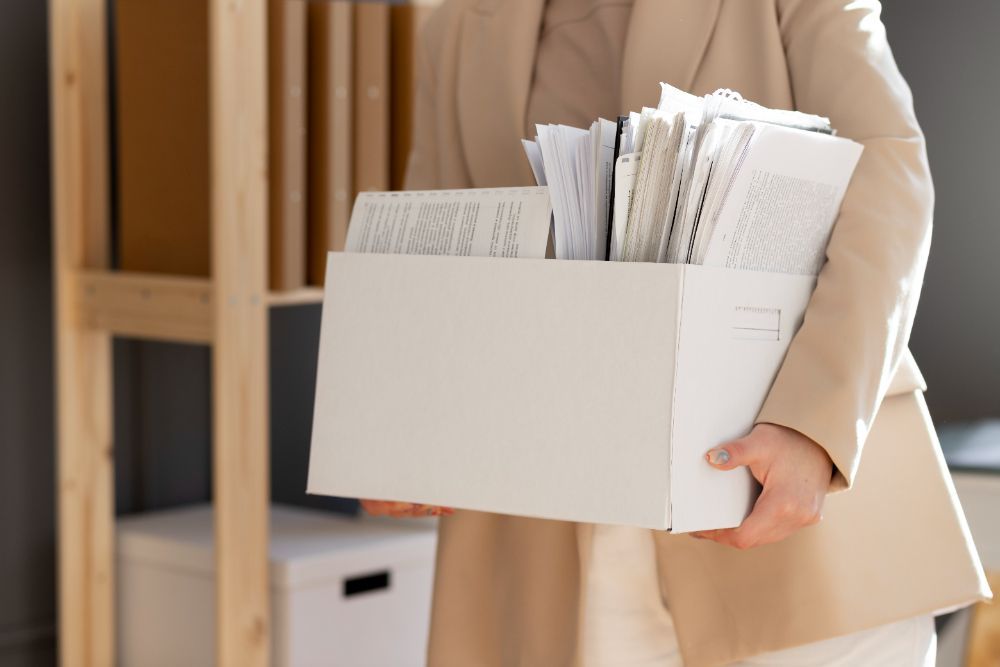 A woman is holding a box of papers in her hands.