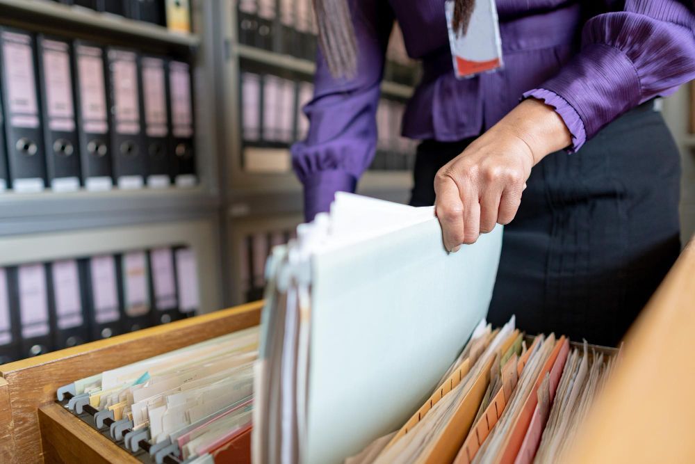 A woman is taking a piece of paper out of a filing cabinet.