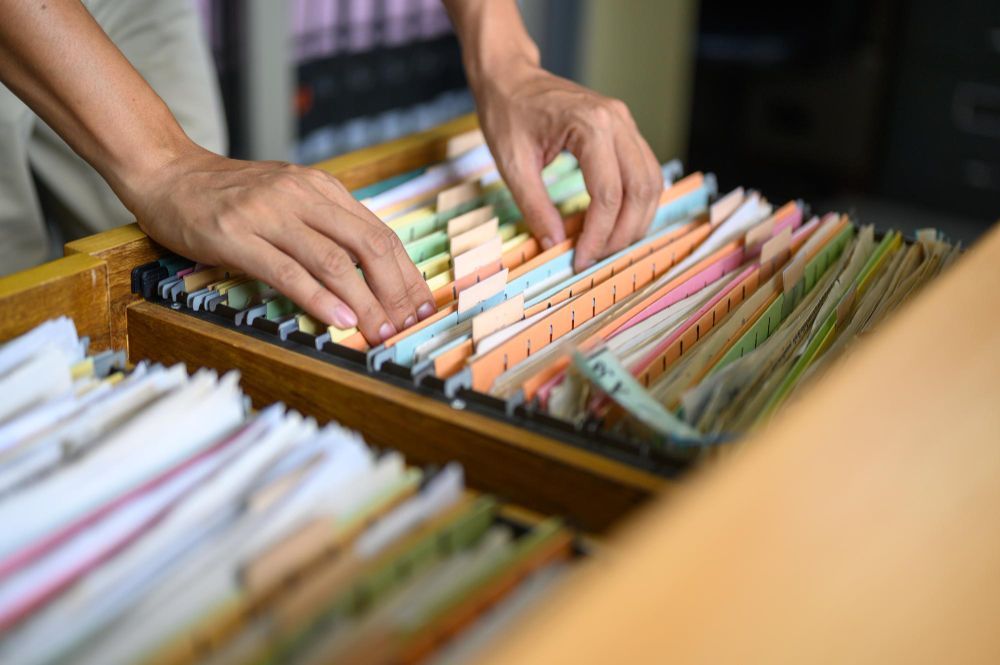 A person is looking through a filing cabinet full of papers.