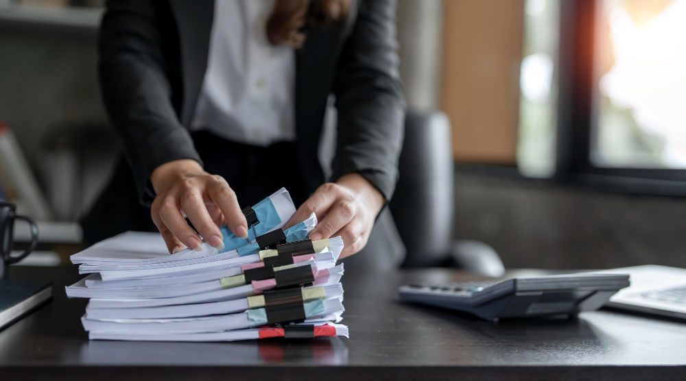 A woman is stacking papers on top of each other on a desk.