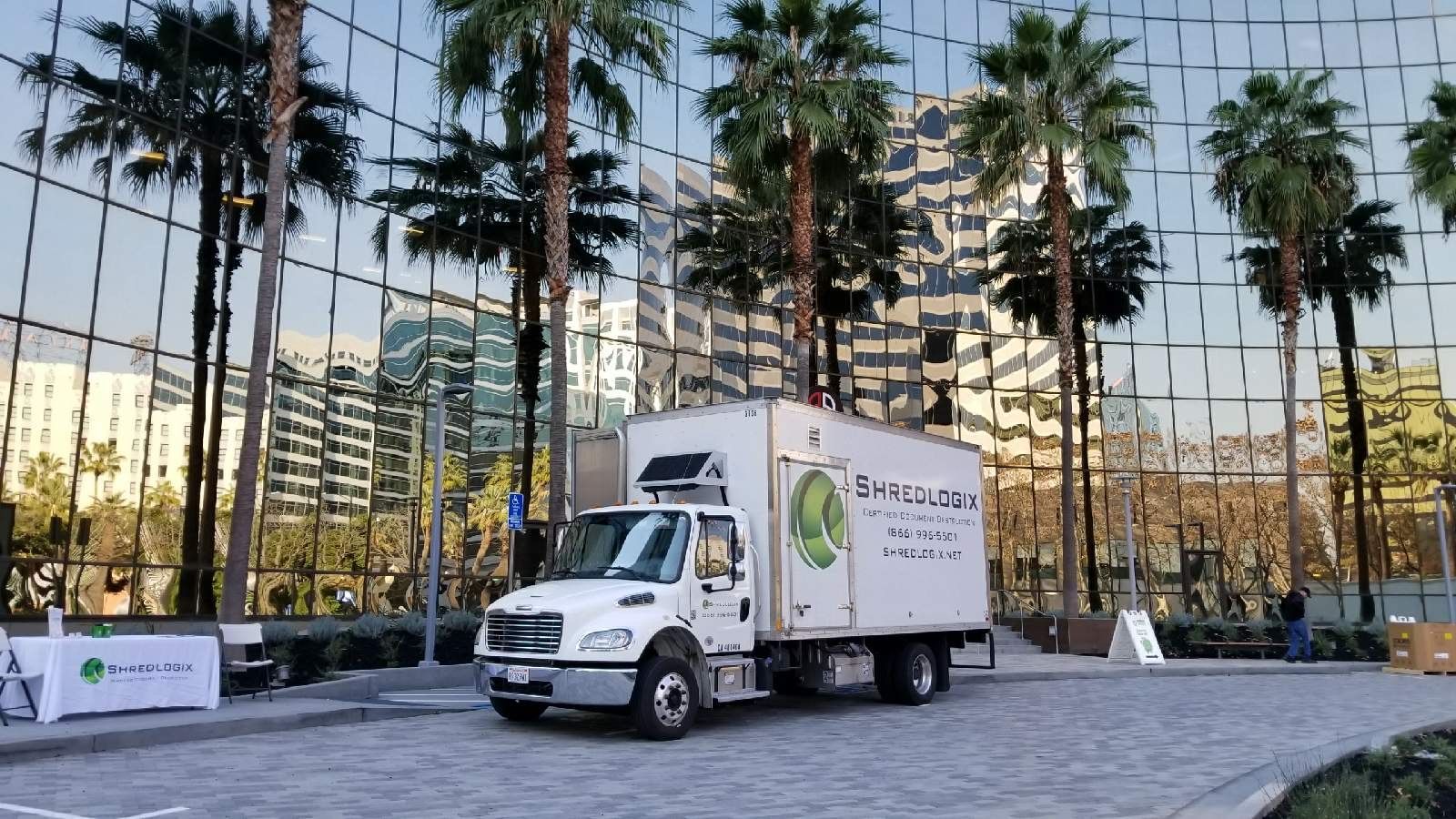 A white truck is parked in front of a building with palm trees.