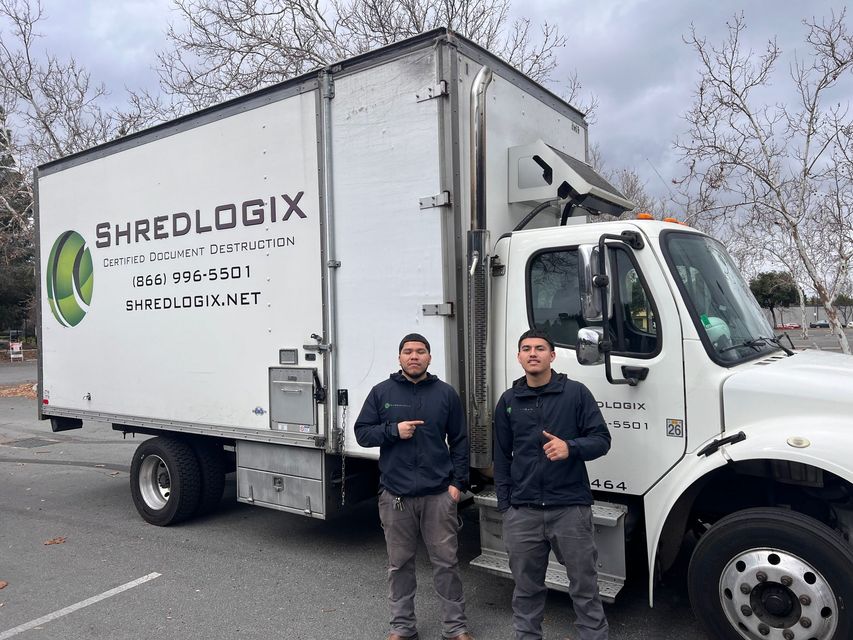 Two men are standing in front of a shredlogix truck.