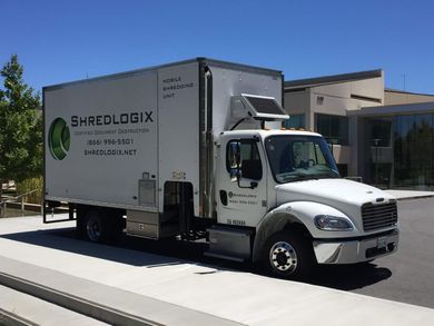A white shredlogix truck is parked on the side of the road.