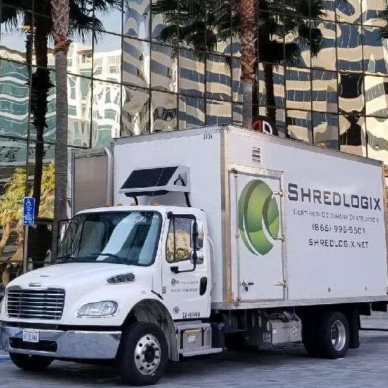 A white shredlogix truck is parked in front of a building