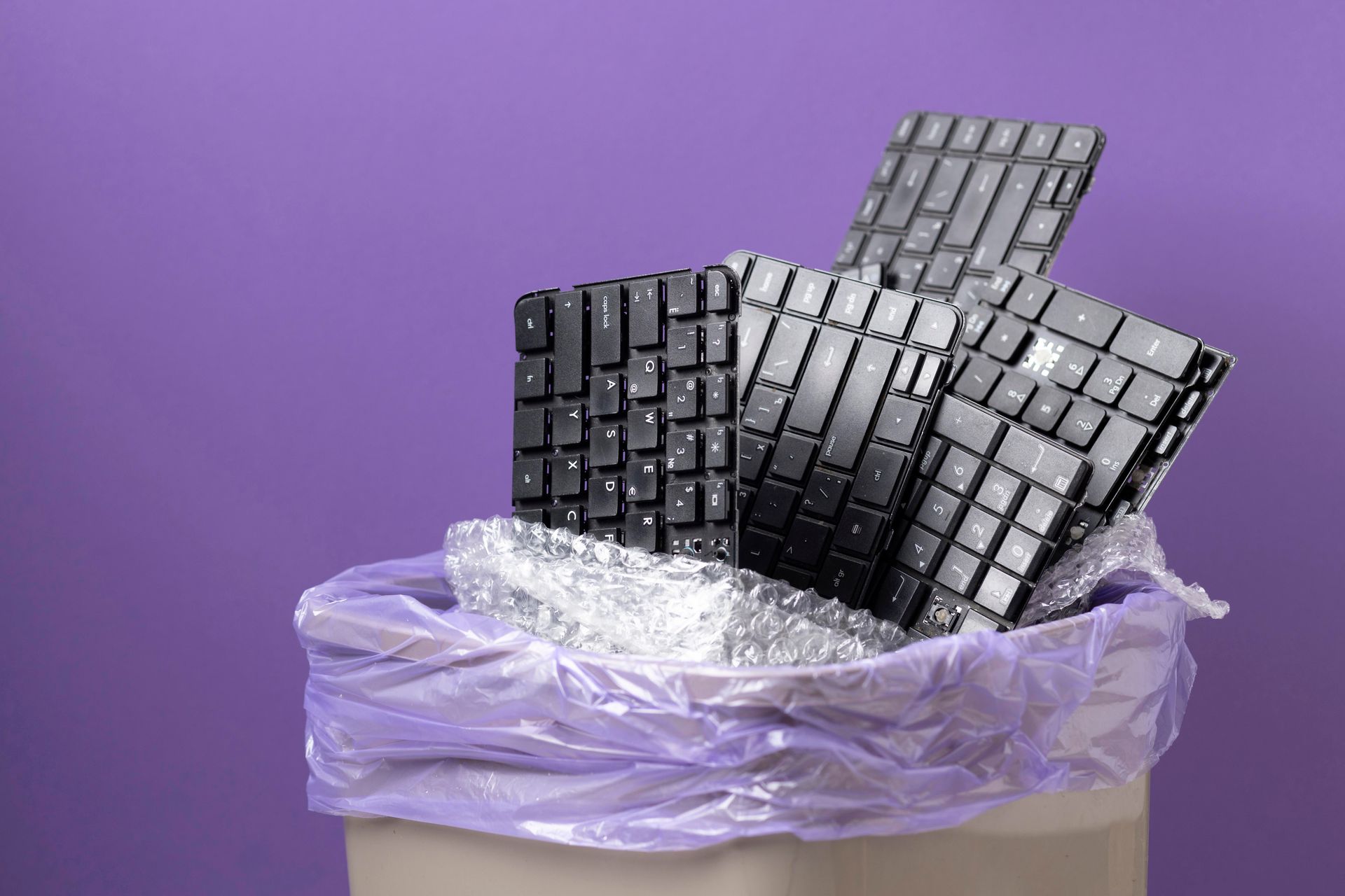 Keyboards piled in a purple trash bag in a waste bin.