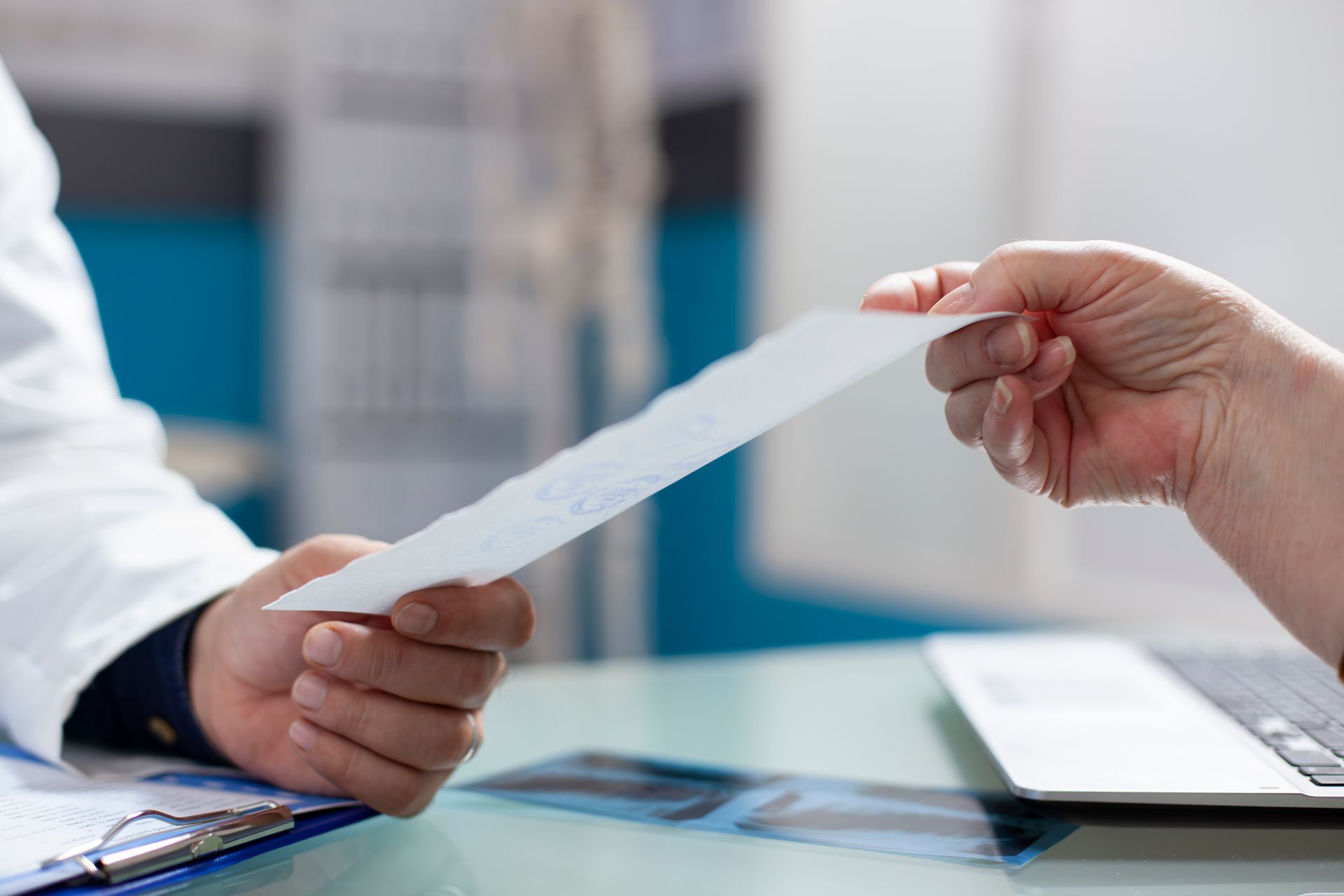 Doctor hands a prescription to a patient over a desk in a medical office.