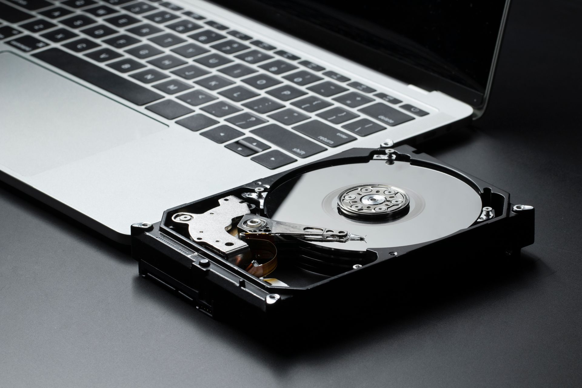 Laptop with opened hard drive next to its keyboard on black surface.