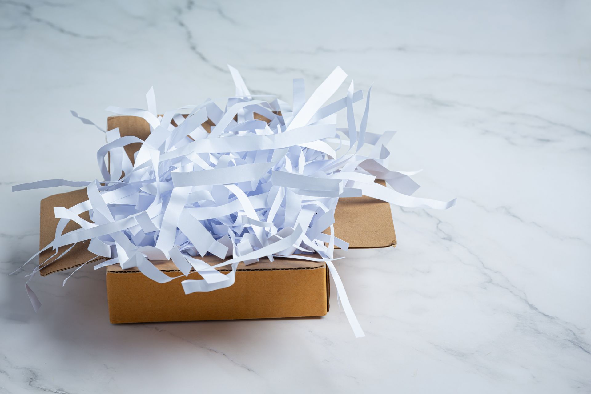 Brown cardboard box filled with white shredded paper, on a marble surface.