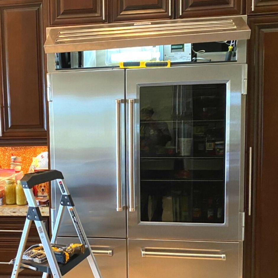 Stainless steel built-in refrigerator in a kitchen, with a step ladder in front and wood cabinets above.