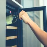 Hand inserting a wine bottle into a glass-door wine cooler
