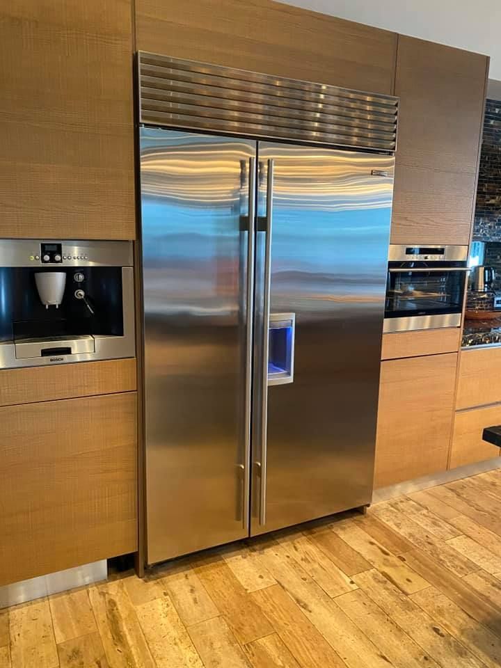 Modern kitchen with stainless steel side-by-side refrigerator flanked by built-in wood cabinetry and ovens.